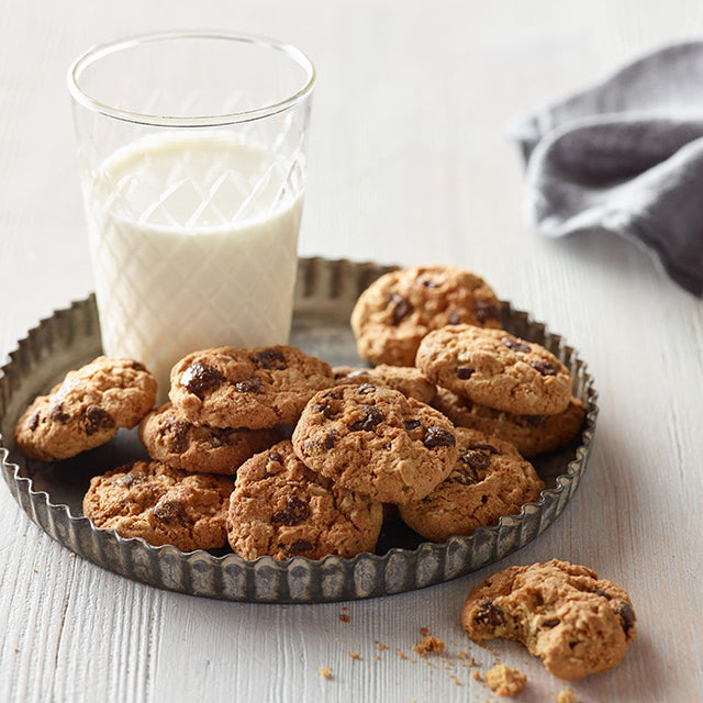 xCookies on a metal tray with a glass of milk on a light wooden surface.