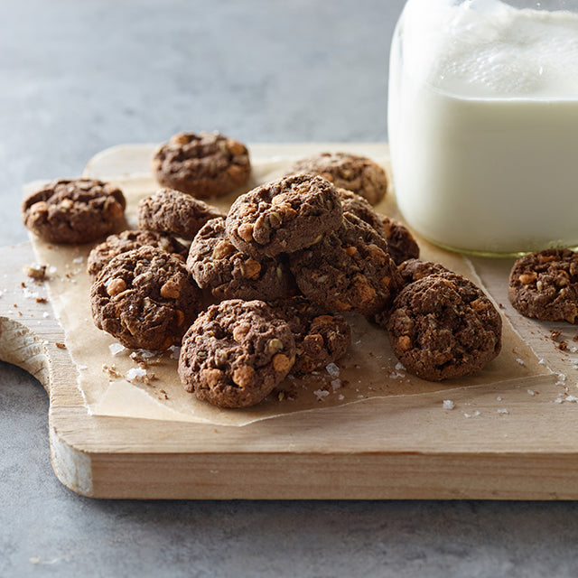 Cookies on a wooden cutting board with a glass of milk on a light gray background