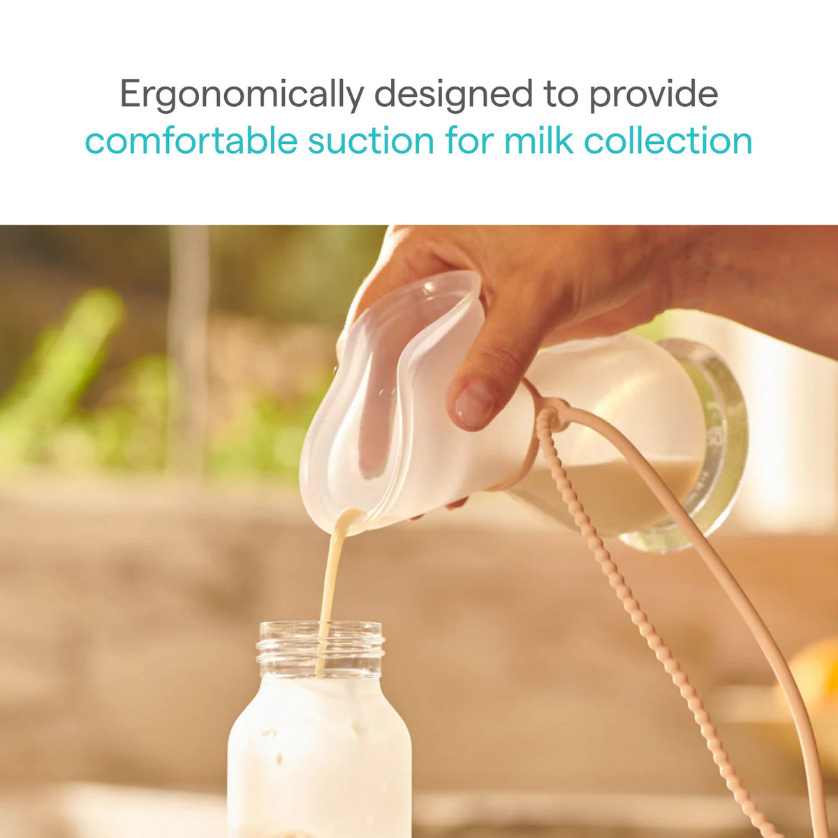 Ergonomically designed milk collection device being used to pour milk into a jar with a blurred natural background.