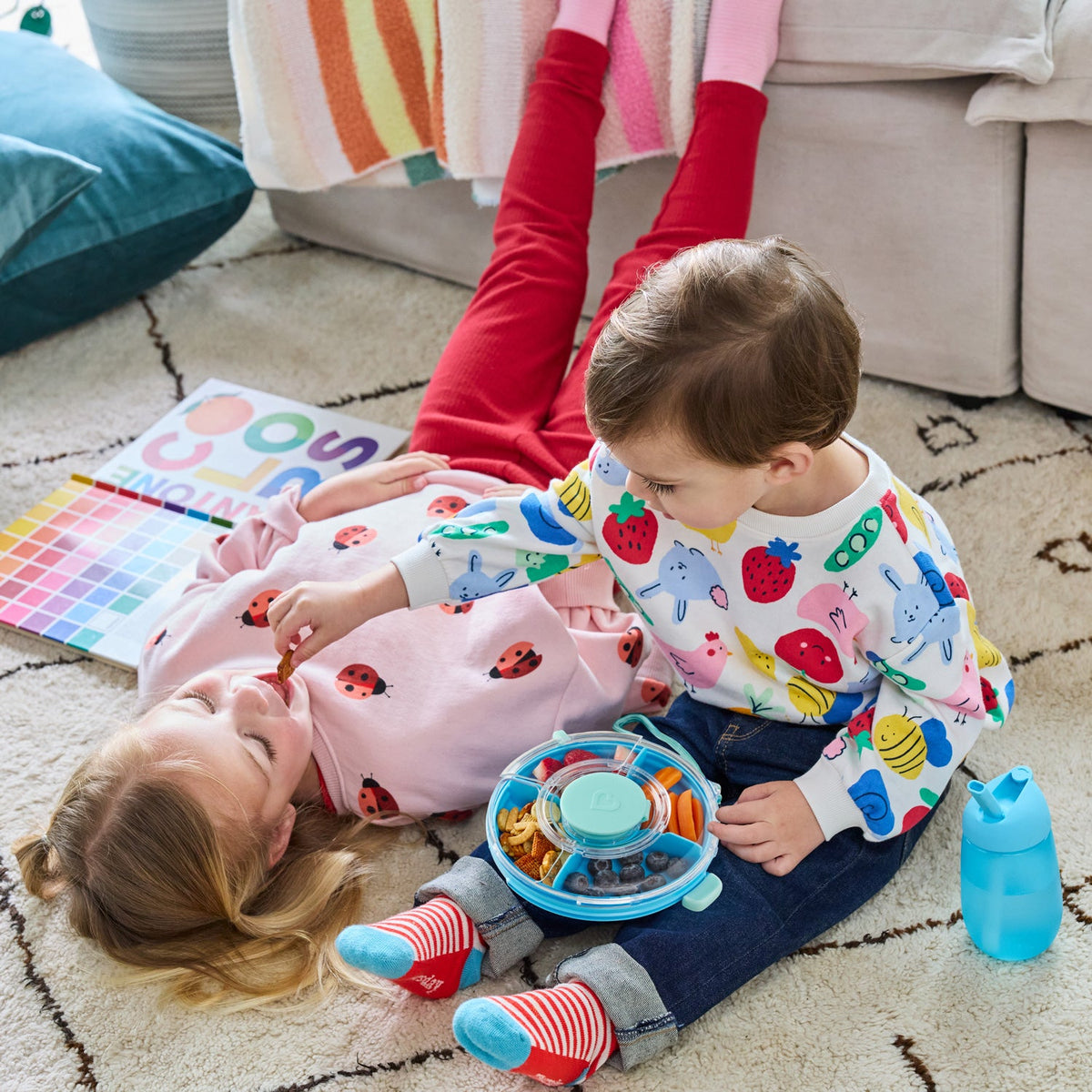 Two children playing on the floor with a colorful toy, surrounded by a cozy living room setting.