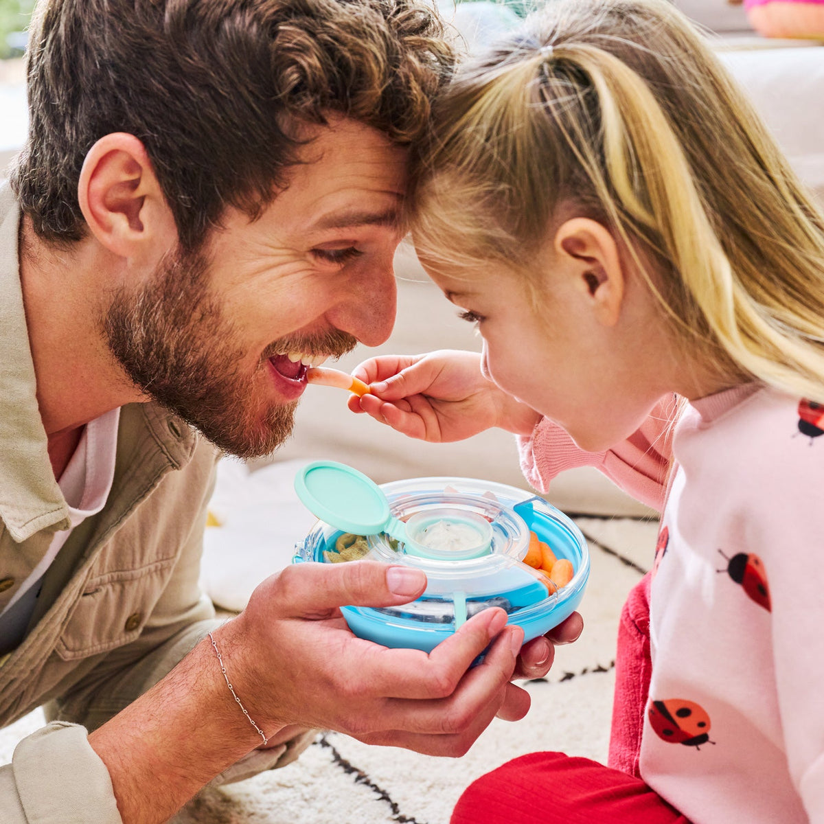 Man and young girl sharing a snack from a blue container on a couch.
