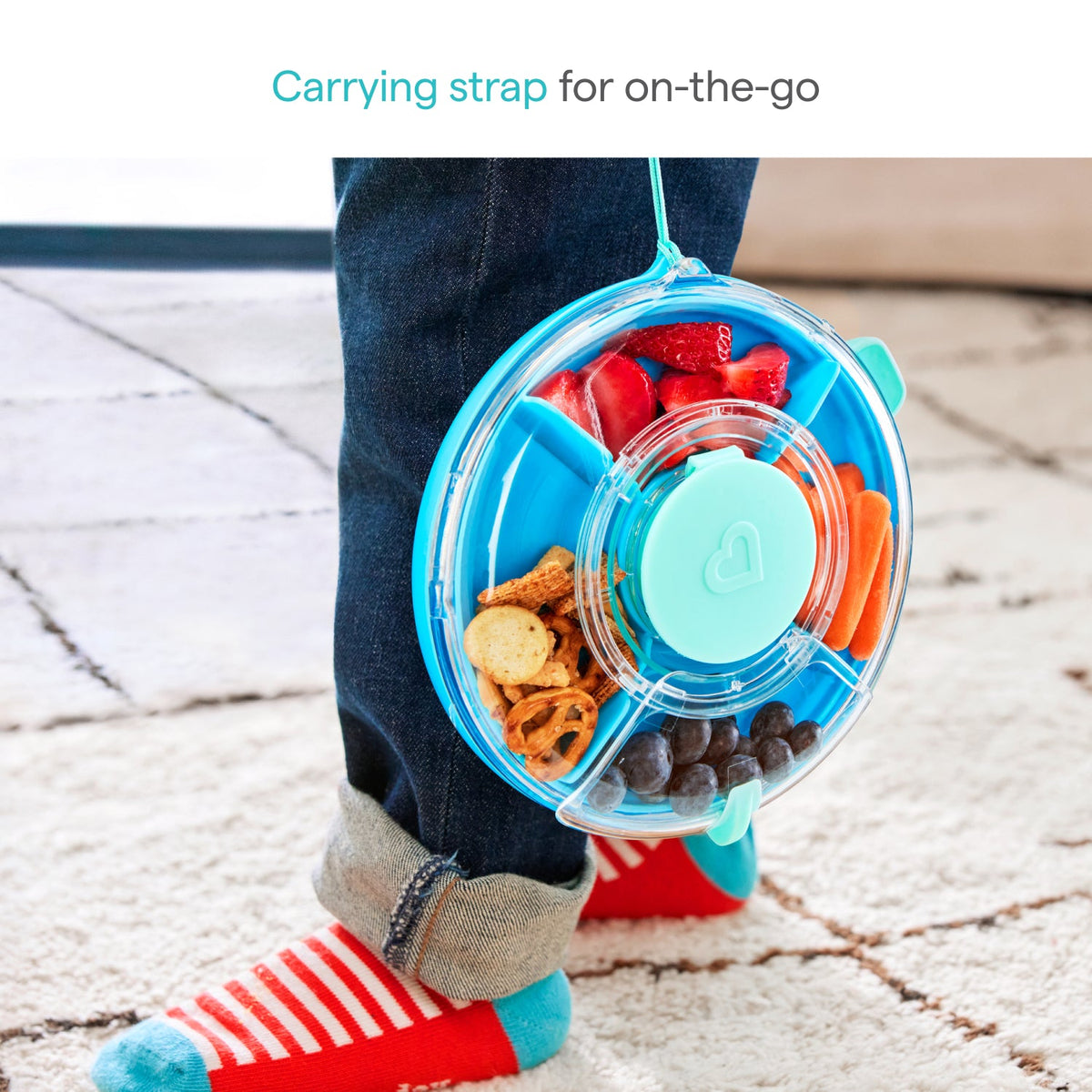 Children's snack container with a carrying strap, filled with snacks, on a sidewalk.